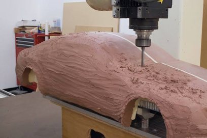 CNC milling machine cutting a new clay model from updated computer data, returning the refined digital design back to a physical form for evaluation