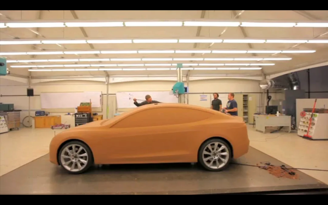 Full orange clay car model in a professional design studio, showing the finished hybrid result where clay and digital tools together produce a stronger design than either method alone